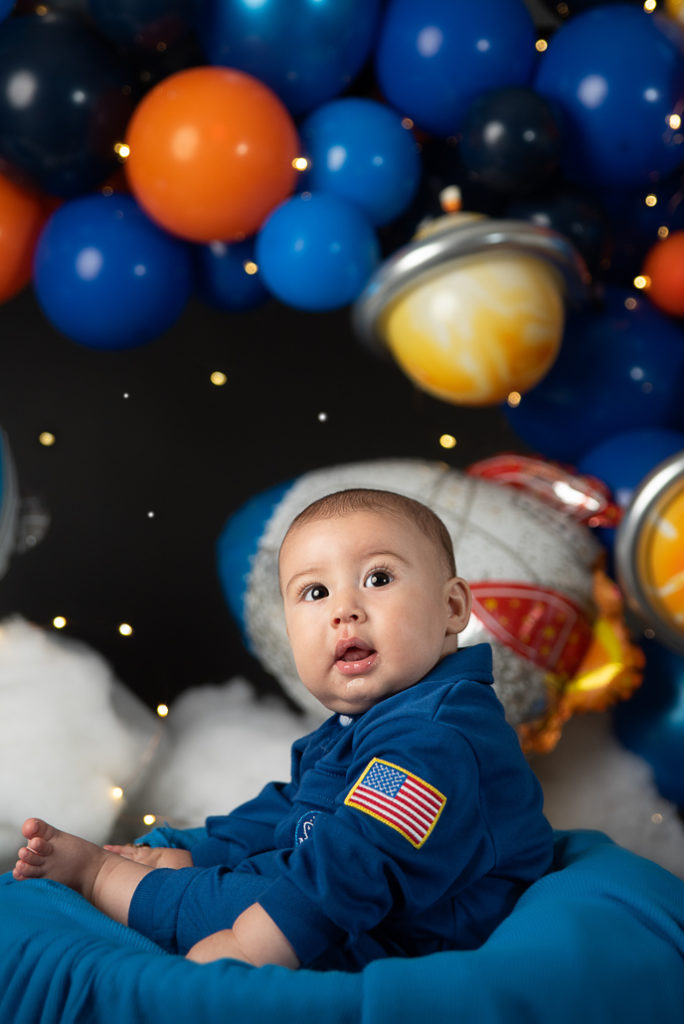 Baby boy in astronaut suit during space-themed first birthday photoshoot with planets backdrop