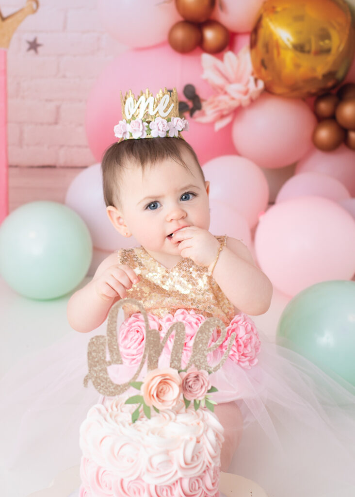 Close-up of baby girl with “One” crown and pink rosette cake in front of her