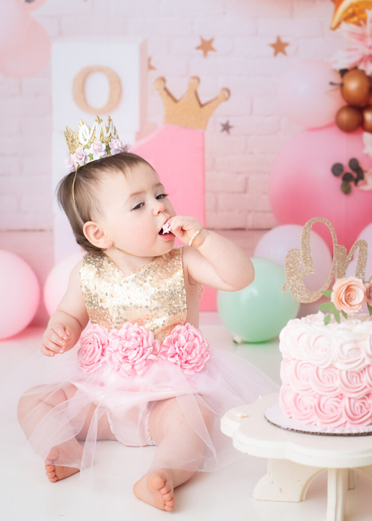 Birthday girl tasting frosting while sitting beside her pink and gold cake