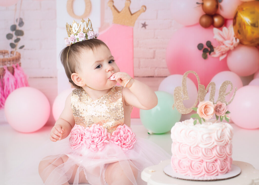 Birthday girl tasting frosting while sitting beside her pink and gold cake