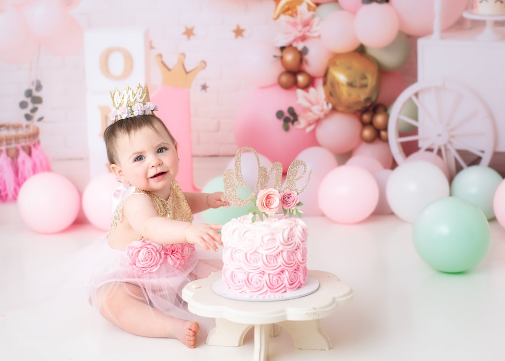 Smiling baby reaching for her cake during a princess-style first birthday photoshoot