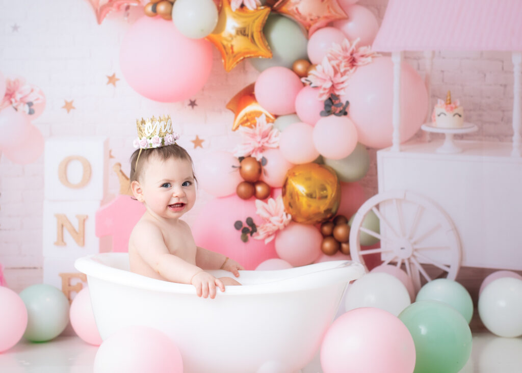 Baby girl smiling in white clawfoot tub after her princess cake smash