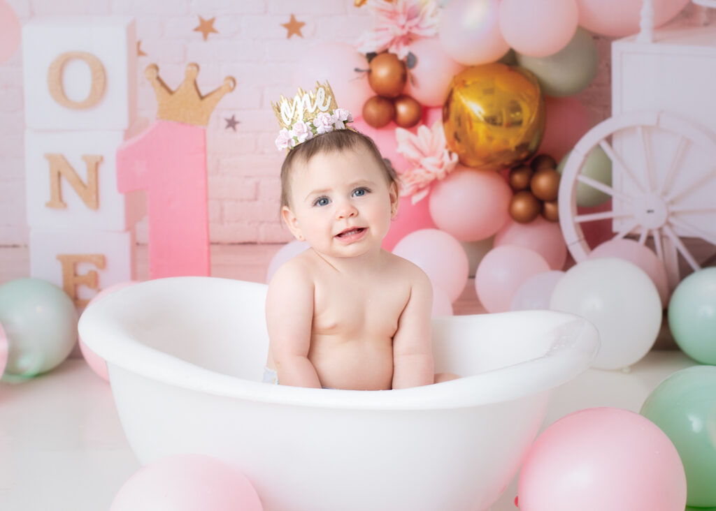 Baby girl smiling in white clawfoot tub after her princess cake smash