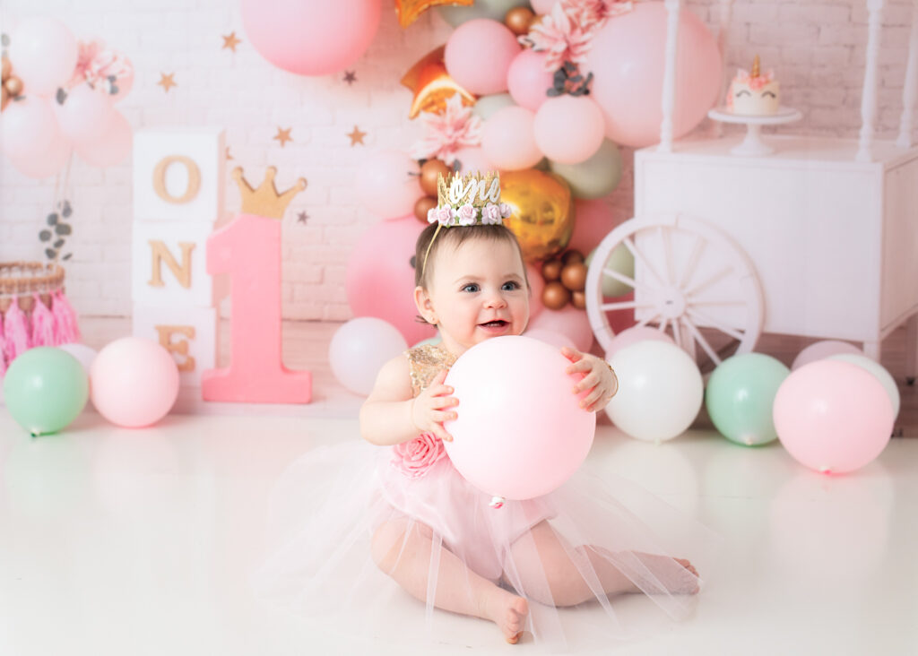 Birthday girl looking up while holding a pink balloon, wearing a crown and tulle skirt