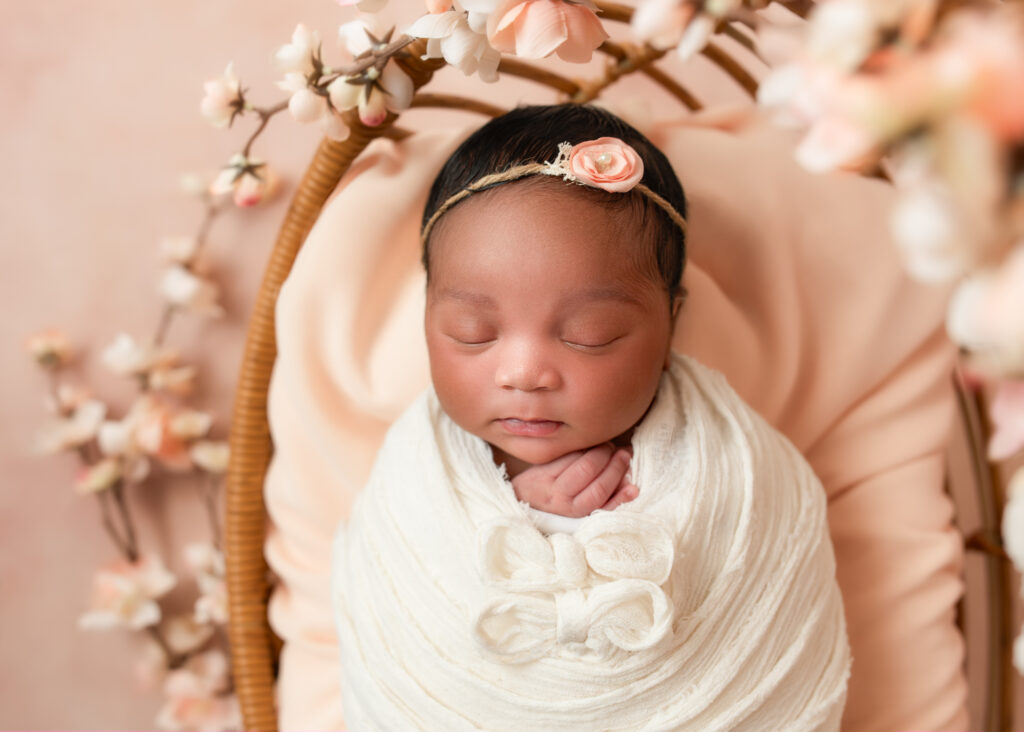 Baby girl in ivory wrap on peach cushion, surrounded by cherry blossom florals