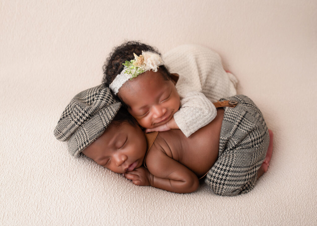 Twin babies in cream outfits, cuddled together on a white couch