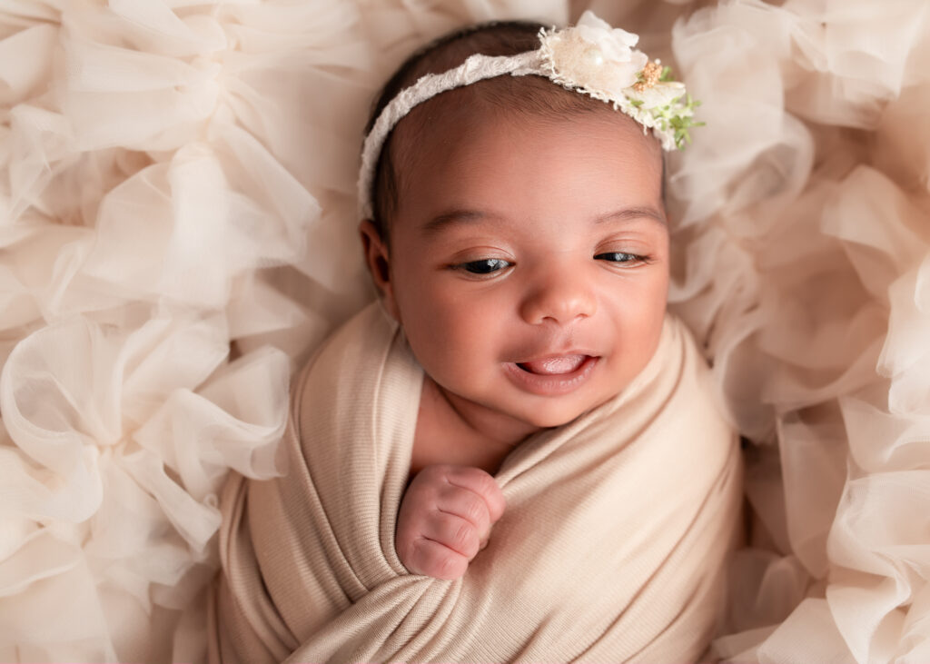 Wrapped baby girl smiling, wearing ivory wrap and floral headband