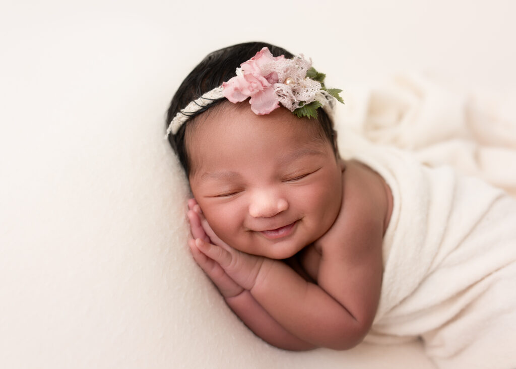 Smiling newborn girl in ivory wrap and pink floral headband