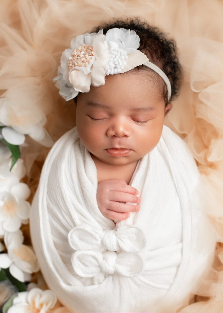 Newborn girl in white wrap with bow, sleeping on floral backdrop