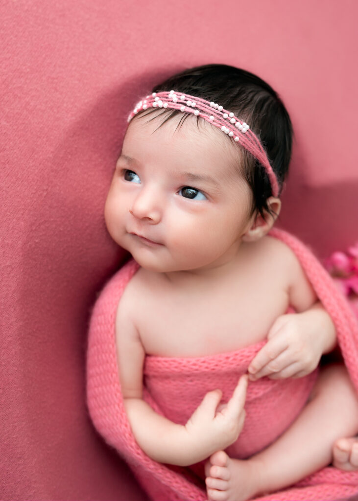 Close-up of baby girl in coral wrap, looking upward with headband
