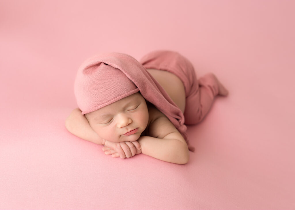 Girl baby posed in light blush wrap with matching hat, sleeping peacefully