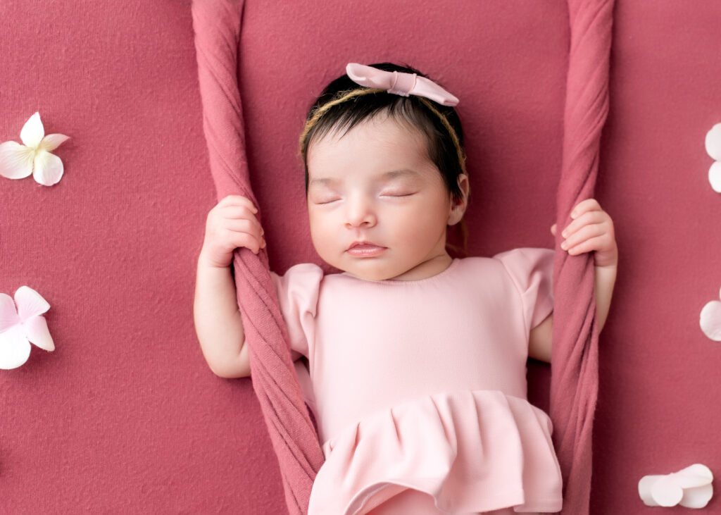 Girl baby in soft blush dress, posed in a fabric swing with white florals

