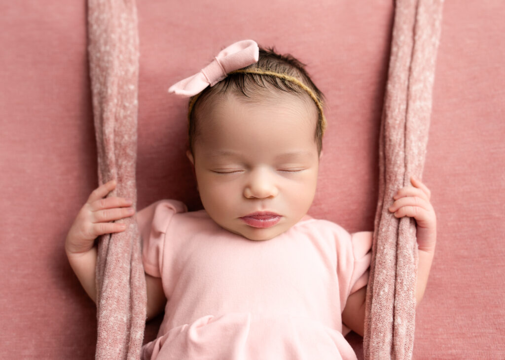 Baby girl in pale pink bow headband, laying on rose-toned fabric