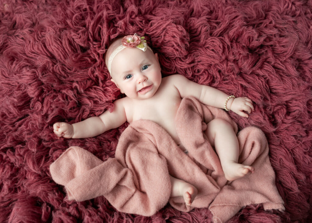 Smiling baby girl wrapped in mauve tones, lying on textured flokati