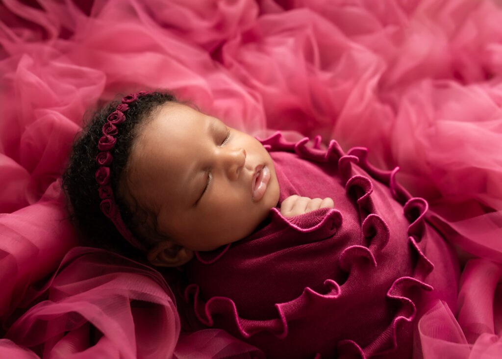 Sleeping baby girl in deep pink ruffles, wrapped on fluffy backdrop


