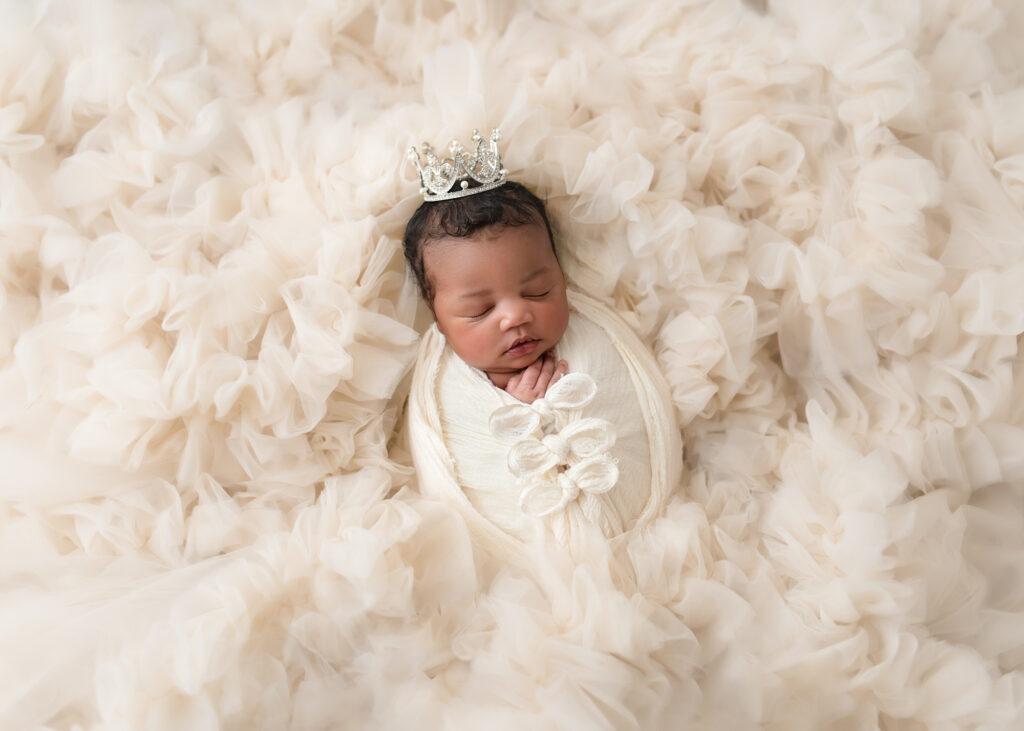 Baby girl in a floral wrap and headband, lying on cream flokati