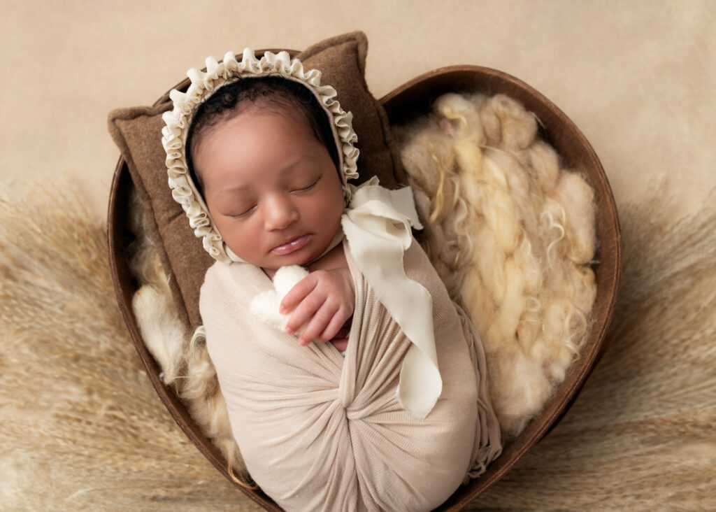 Newborn girl swaddled in white, sleeping in a heart-shaped basket