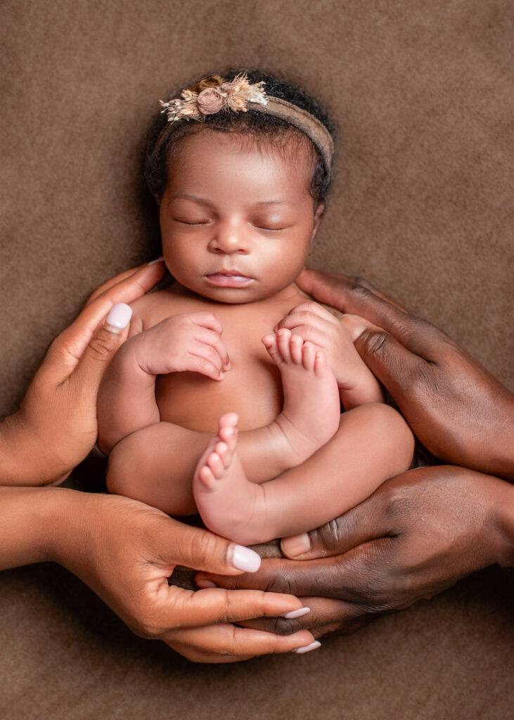 Newborn in parent’s hands, posed with arms and legs tucked in