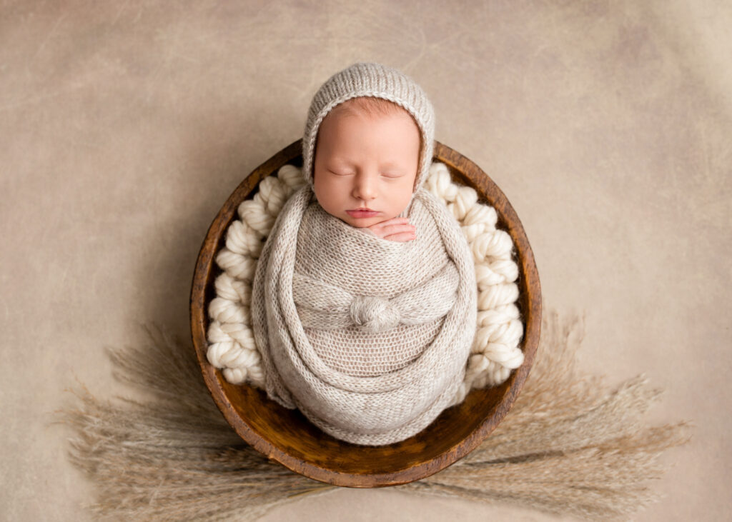 Newborn baby wrapped in neutral knit swaddle, posed in a wooden bowl with pampas grass at Misty Dawn Photography studio in Birmingham, AL