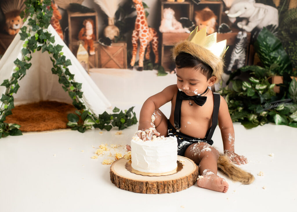 First birthday boy taste-testing cake during jungle cake smash setup