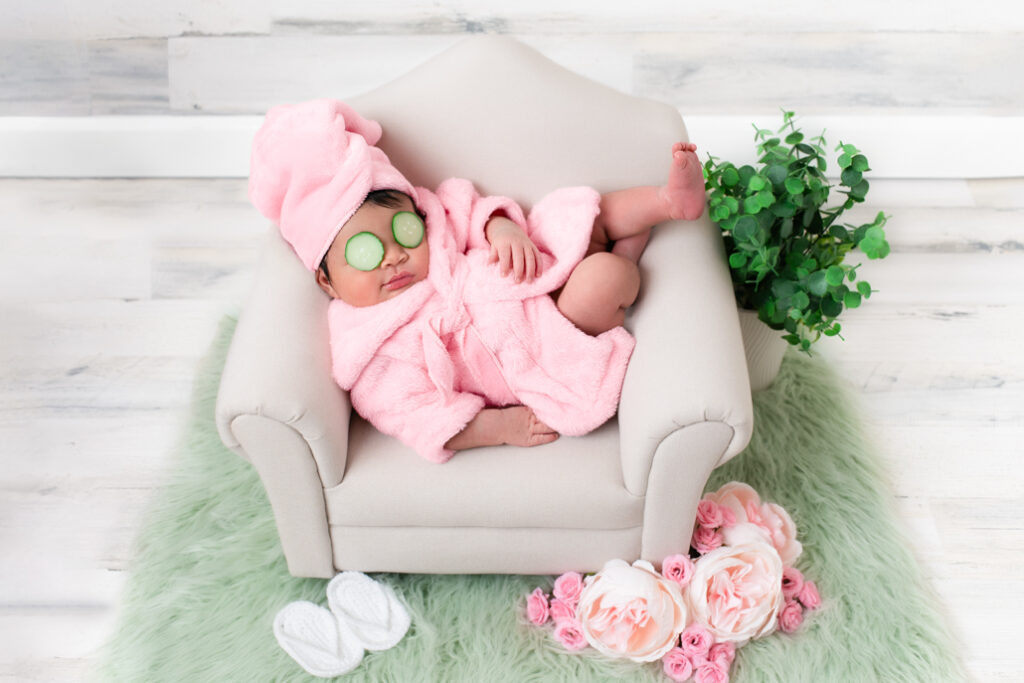 Newborn baby girl dressed in a pink robe, styled in a spa-themed studio photo session in Birmingham, Alabama.