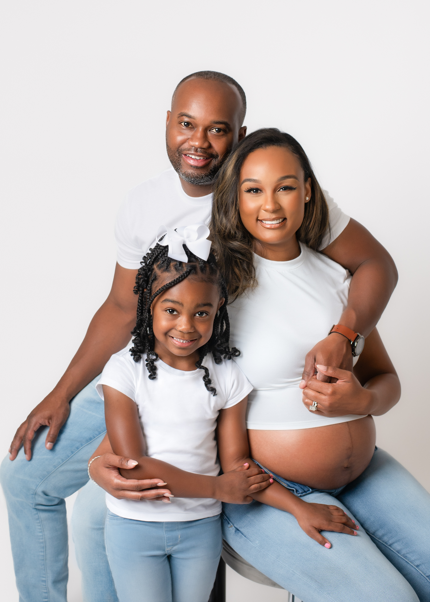 Pregnancy portrait of a glowing family in coordinated outfits—expectant mother seated with partner and child in a bright Birmingham studio, celebrating connection and new life.