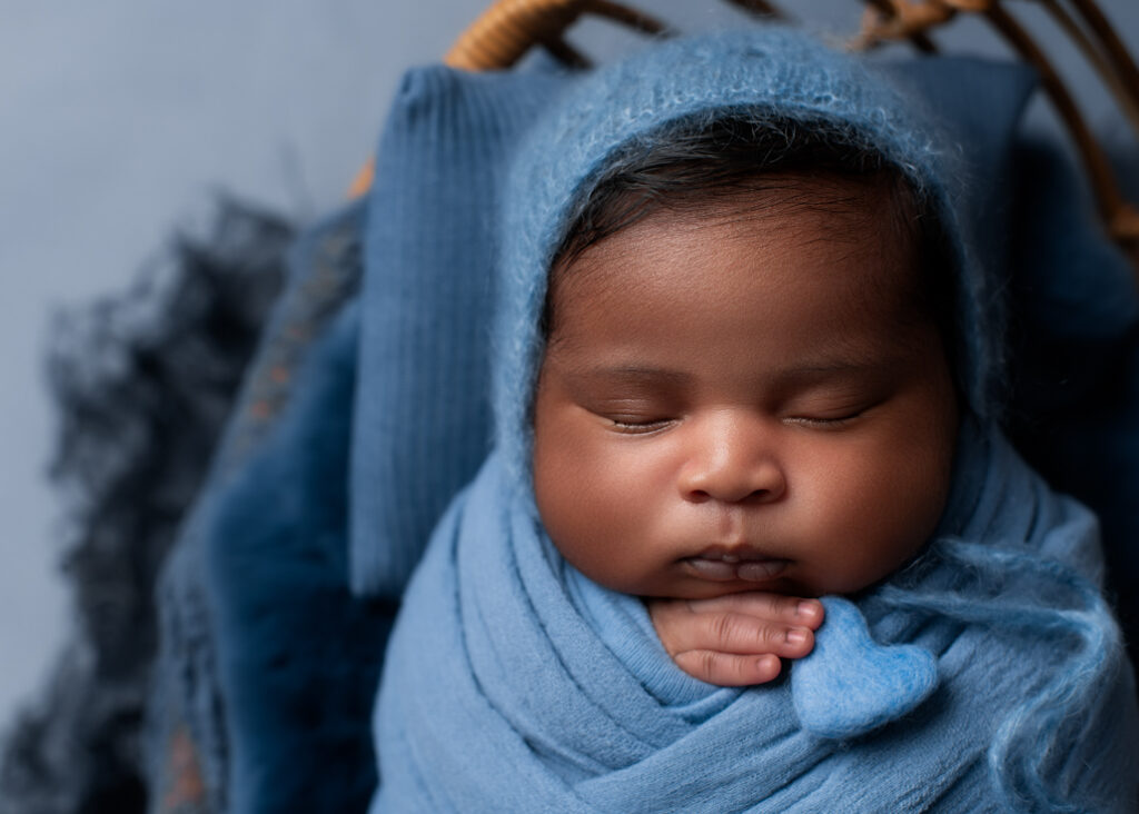 boy baby photo wrapped in blue with blue bonnet and blue texture holding a heart