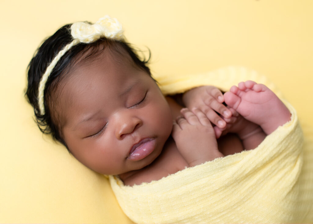 a newborn picture in Alabama wrapped in yellow laying on a yellow background sleeping