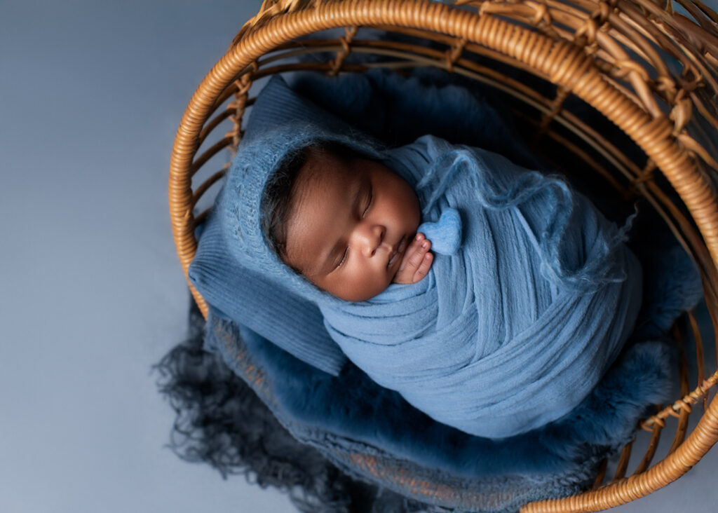 boy baby photo in a wicker basket wrapped in blue with blue bonnet and blue texture holding a heart