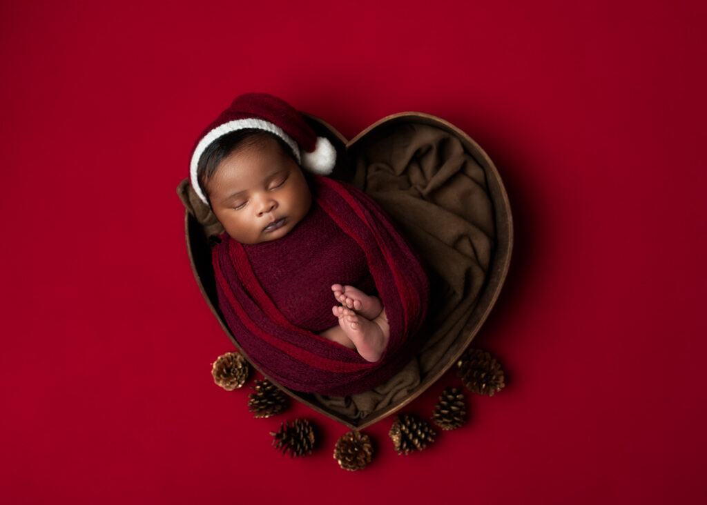 baby wrapped in red with a red sleepy hat with white ball on end in a heart with red background