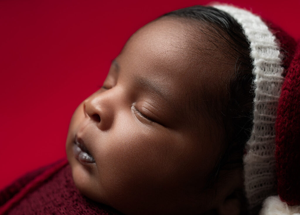 a closeup of baby wrapped in red with a red sleepy hat with white ball on end in a heart with red background