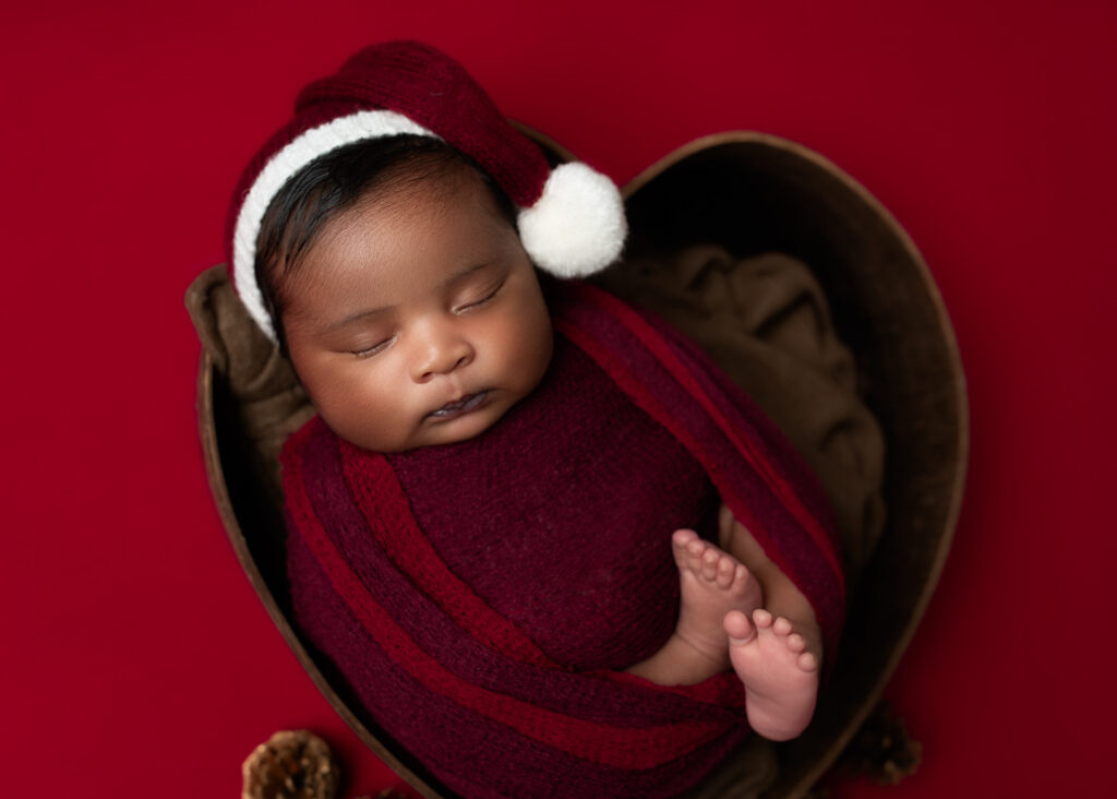 baby wrapped in red with a red sleepy hat with white ball on end in a heart with red background