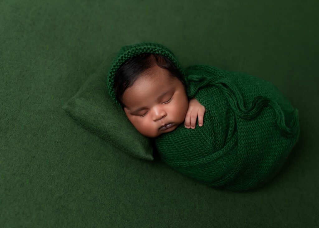 baby sleeping on green fabric, green pillow, and wrapped in green with a green bonnet