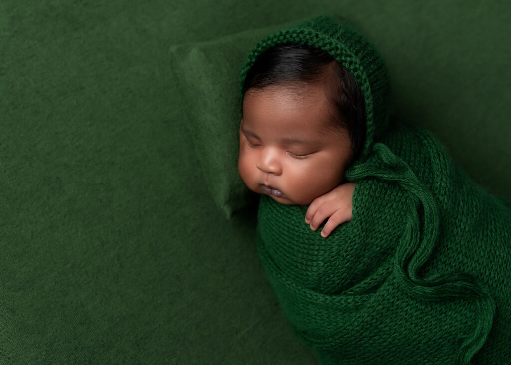 baby sleeping on green fabric, green pillow, and wrapped in green with a green bonnet