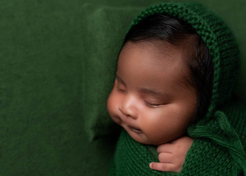 baby sleeping on green fabric, green pillow, and wrapped in green with a green bonnet