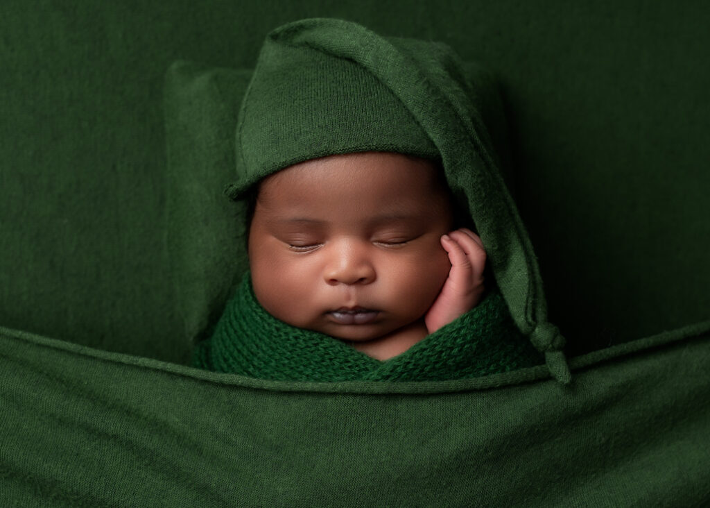 boy baby photo sleeping on green fabric, green pillow, and wrapped in green with a green sleepy hat