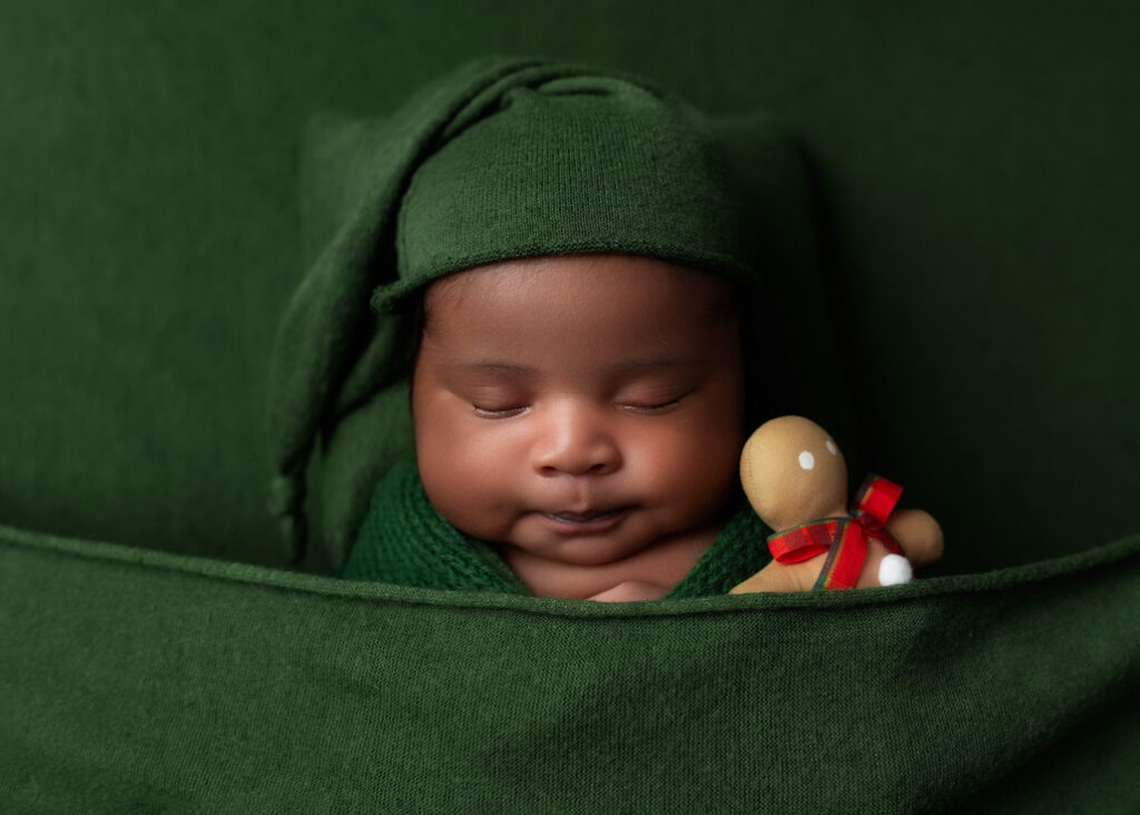 boy baby photo sleeping on green fabric, green pillow, and wrapped in green with a green sleepy hat and a gingerbread man