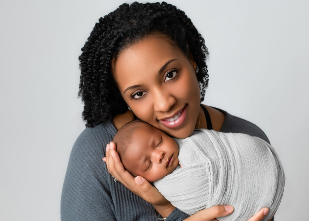 Twins' newborn photography showcasing a beautiful mother cradling her swaddled newborn, smiling with love and warmth. A precious mother-baby moment filled with tenderness