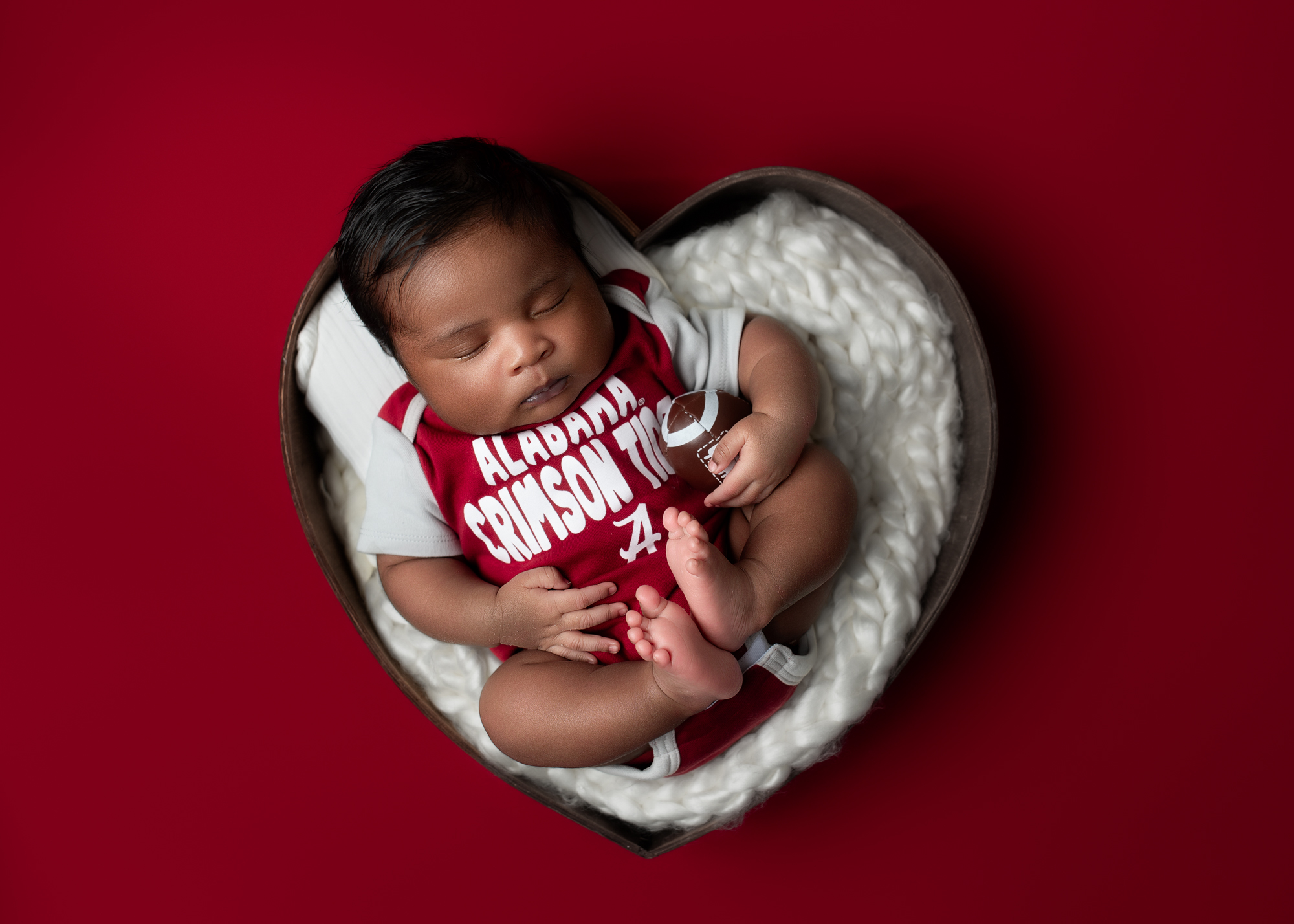 Best baby photos – newborn boy in heart prop with Crimson Tide onesie and soft white blanket, Misty Dawn Photography in Birmingham, AL.