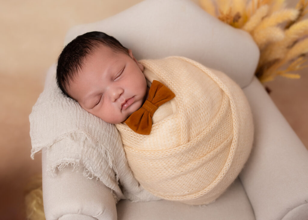 Newborn baby swaddled in soft cream wrap, sleeping peacefully on a textured blanket at 7 days old.