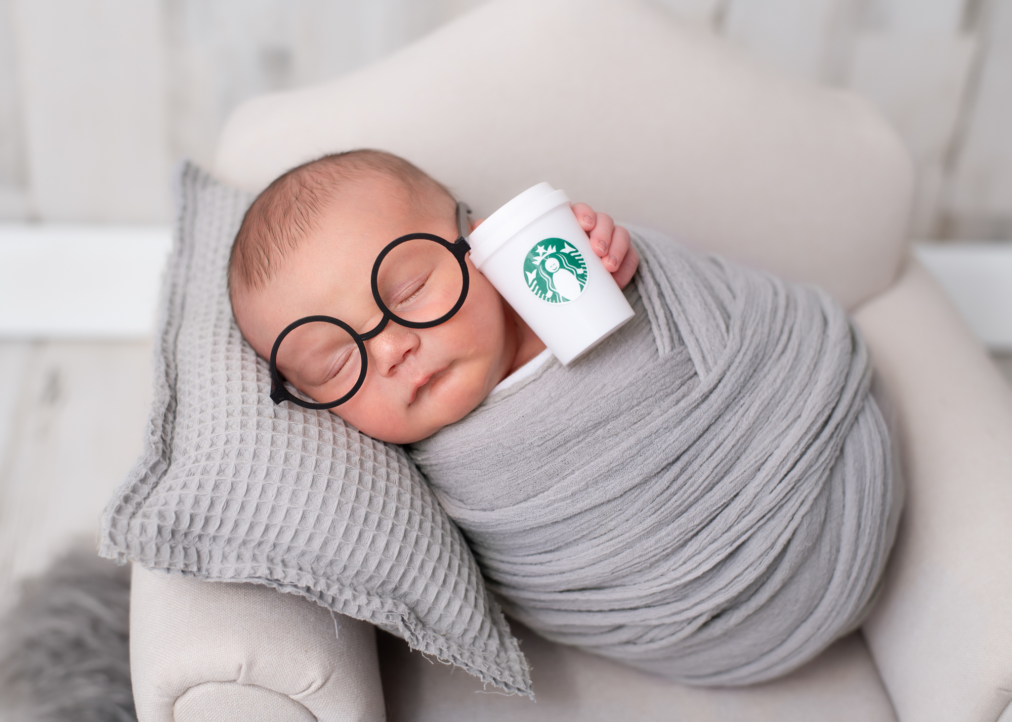 Newborn wrapped in a soft gray blanket wearing round black glasses and holding a small coffee cup prop by Misty Dawn Photography, Birmingham newborn photographer.