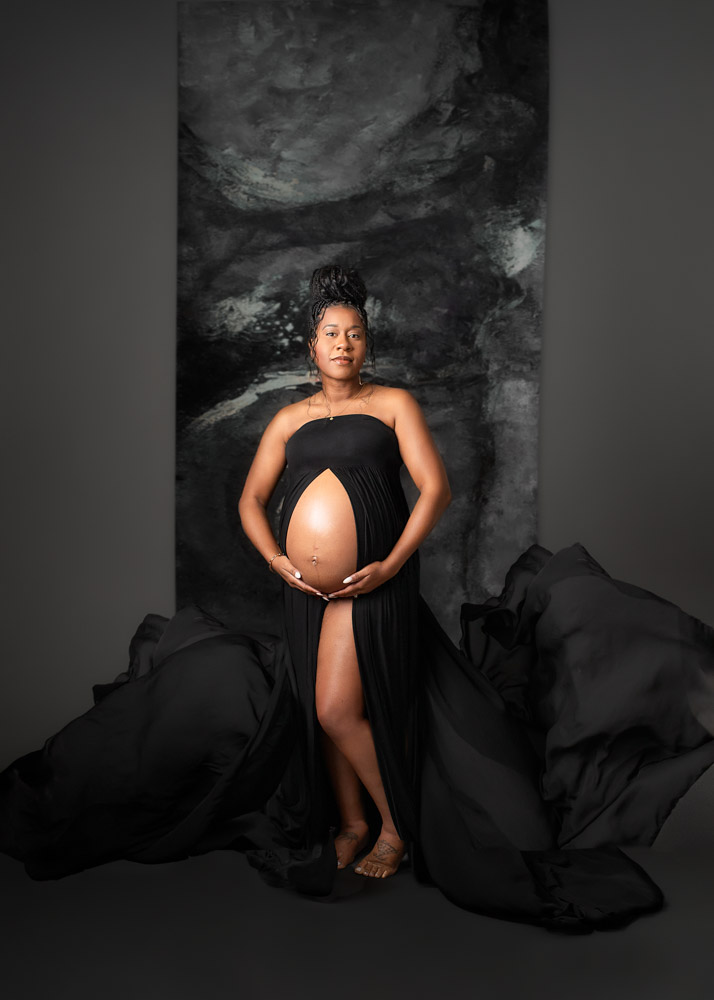 Maternity studio portraits of pregnant woman in black dress that shows off the baby bump and has flowing fabric.