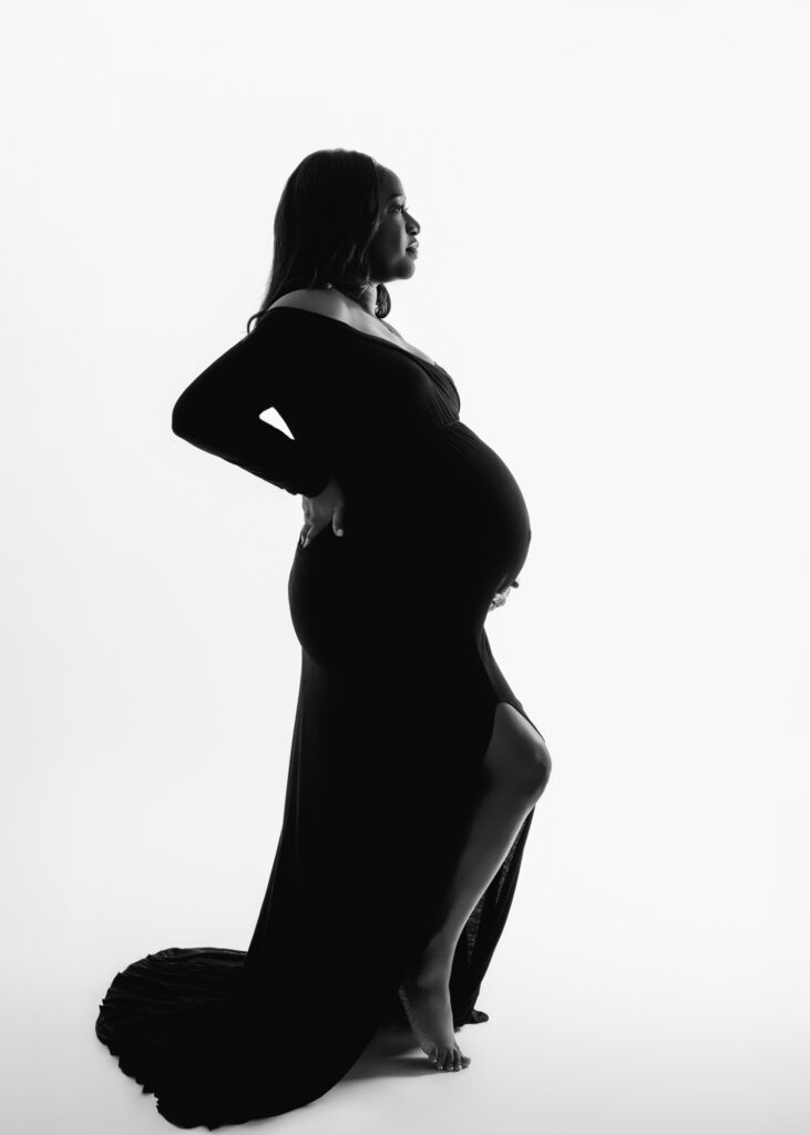 Silhouette of pregnant woman in form-fitting gown, standing in profile with hand on hip and baby bump in view.