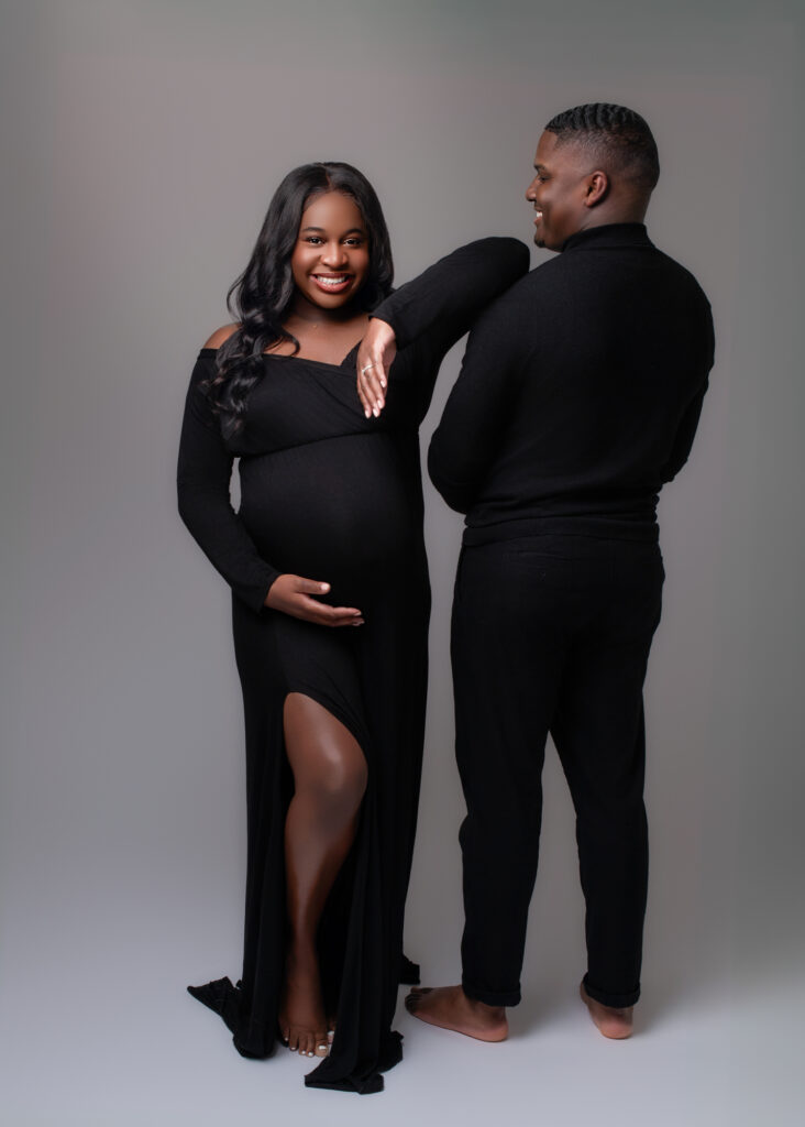 Maternity couple in black attire smiling at the camera, showing connection and confidence.