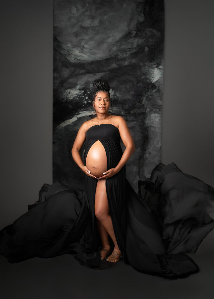 Maternity studio portraits of pregnant woman in black dress that shows off the baby bump and has flowing fabric.