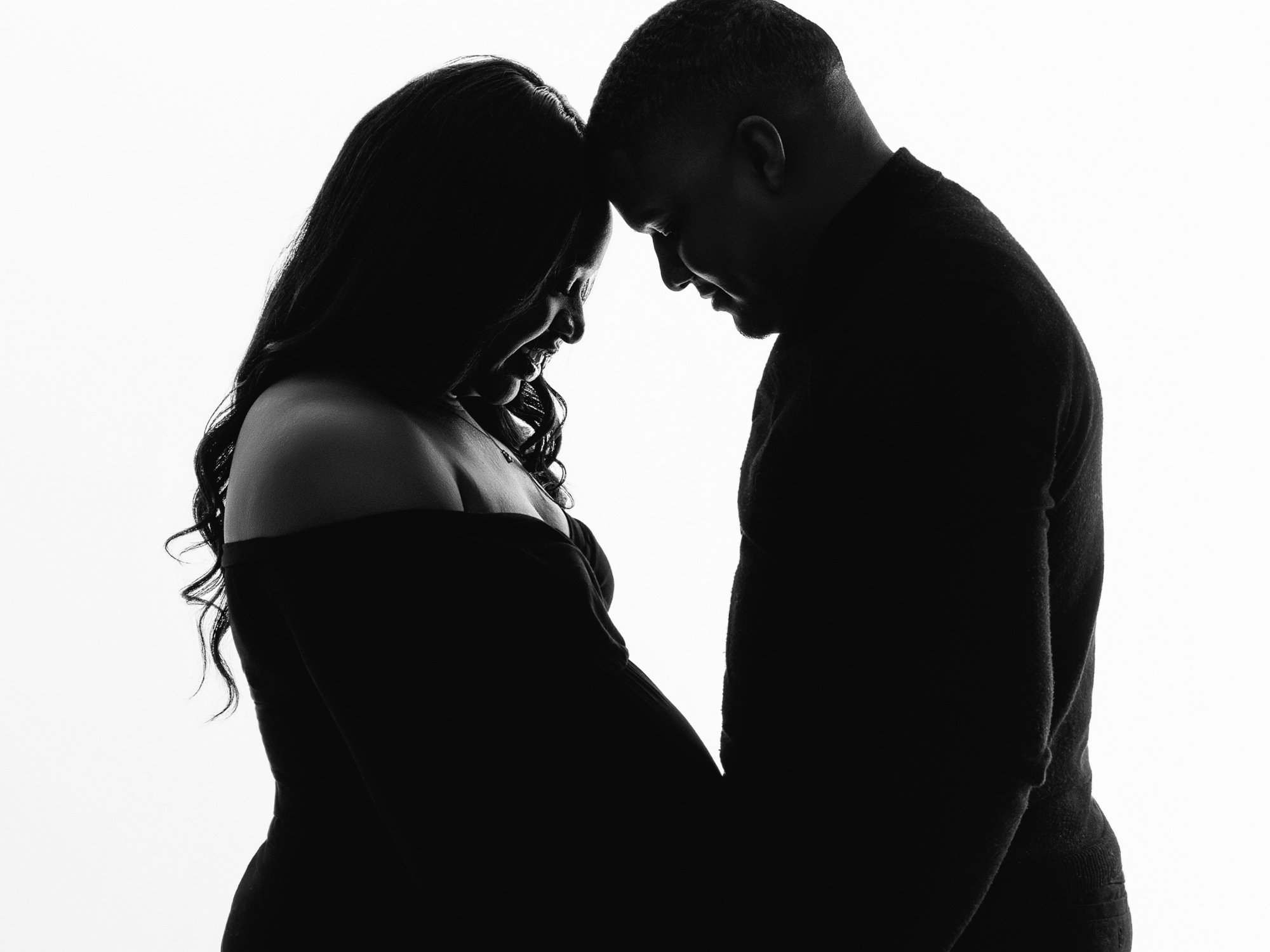 Silhouette of pregnant woman and husband facing each other during a maternity session.