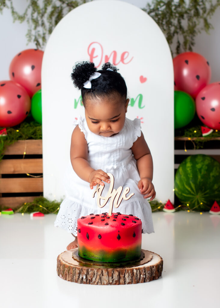 Birthday girl reaching for watermelon cake on rustic wood stand, focused and curious.