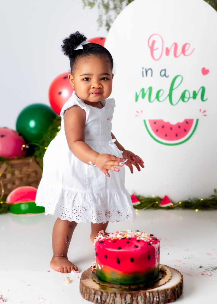 Birthday girl walking toward the camera in white eyelet dress, smiling with balloons behind her.
