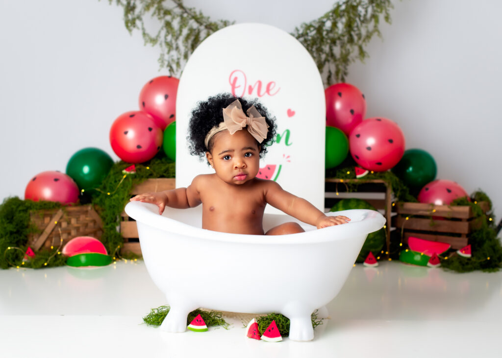 Baby splashing in a white clawfoot tub, surrounded by watermelon decor.