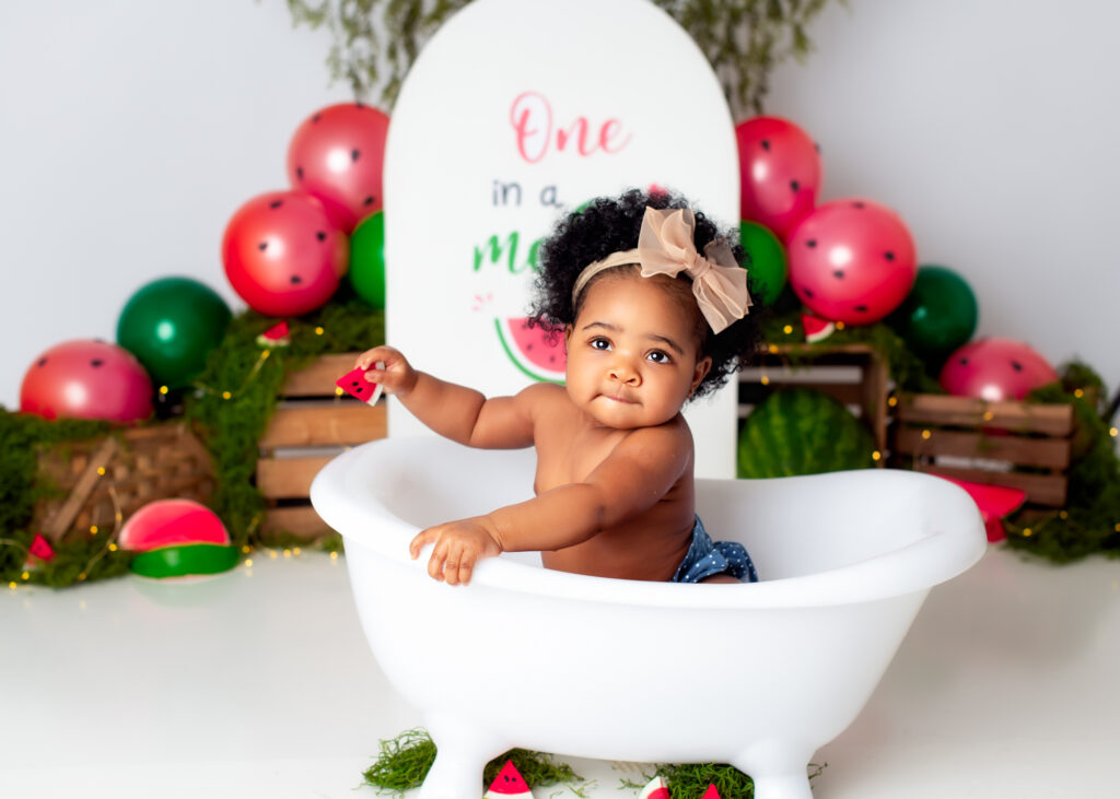 Another angle of baby in white tub, smiling with red and green balloons behind her.